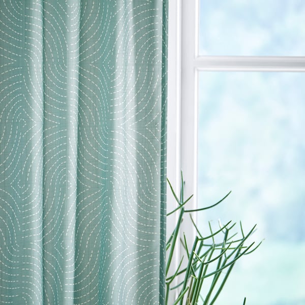 Soft ÅKERMOLKE turquoise curtain with white wavy pattern, blends with plant, frames window. Light-filtering, eco-friendly polyester.