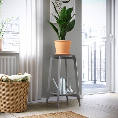 Small plant stand holds tall orange plant by window, near basket.