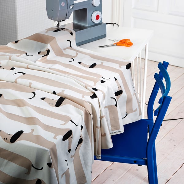 Sewing machine on table with fabric featuring playful dachshunds. Scissors and thread nearby, ready for crafting.