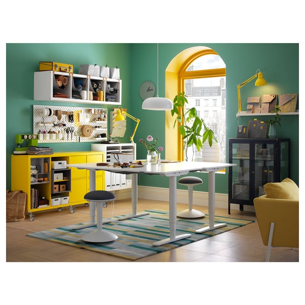 Vibrant home office with BEKANT white adjust. Standing desks, yellow accents, green walls, pegboard & plants.