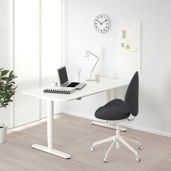 White BEKANT desk with black chair, laptop, lamp, plant.