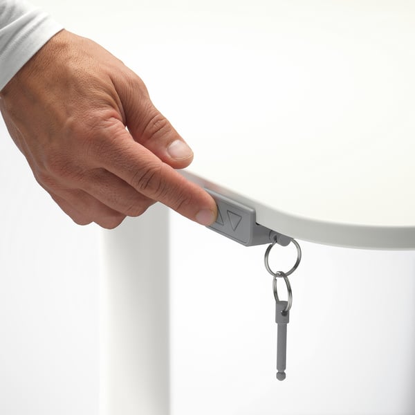 Person adjusting height of BEKANT standing desk using handle, posing key ring.