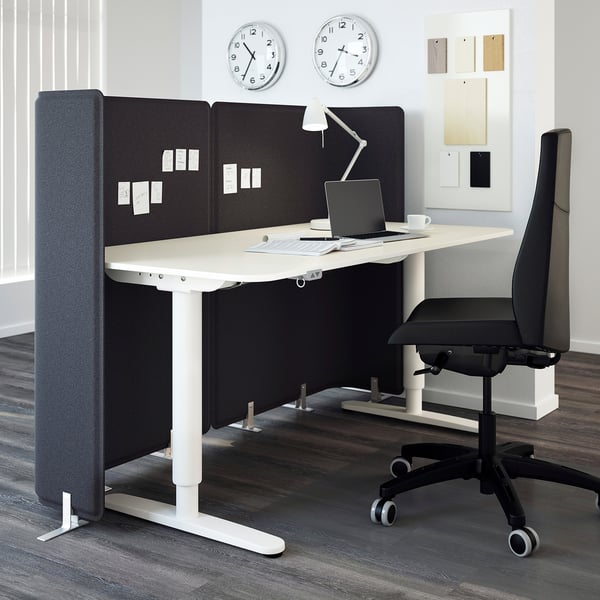 Modern office setup with a large adjustable desk, black office chair, laptop, and grey dividers.