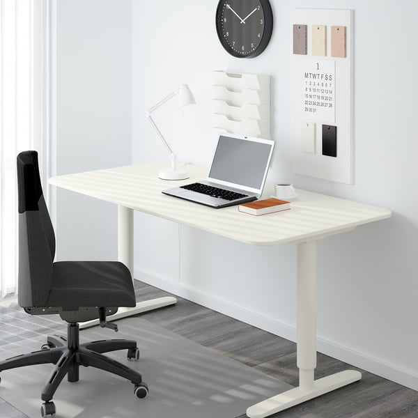 Modern white adjustable height desk with laptop, chair, lamp, and wall calendar.
