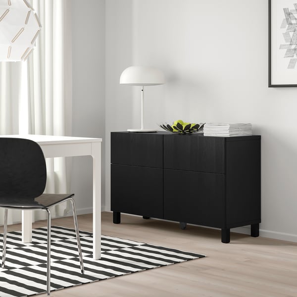 Ikea BESTÅ black storage unit with two doors and drawers. Positioned next to a white table with a black chair.