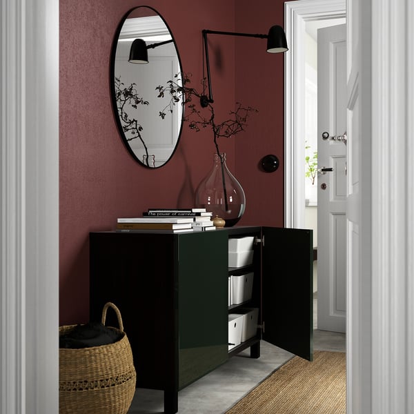 Open sideboard with adjustable shelves shows organised storage. Vase and branches decorate top. Dark walls and minimalist design.