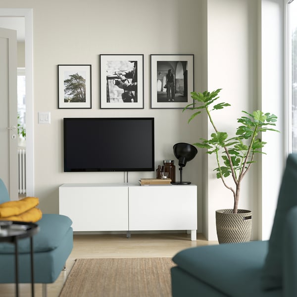 Modern living room with white BESTÅ tv stand, flat screen tv, teal chairs, and large plant. Artwork decoration on wall, cosy atmosphere.