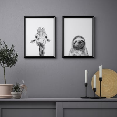 Framed giraffe & sloth prints above shelf with plant, candles, plate.