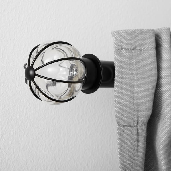 Glass and metal curtain finial mounted on wall, holding light grey curtain.