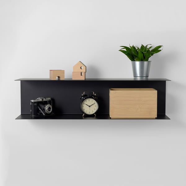 Black wall shelf with camera, clock, wooden box, plant, and small decorative blocks. Displays items neatly.