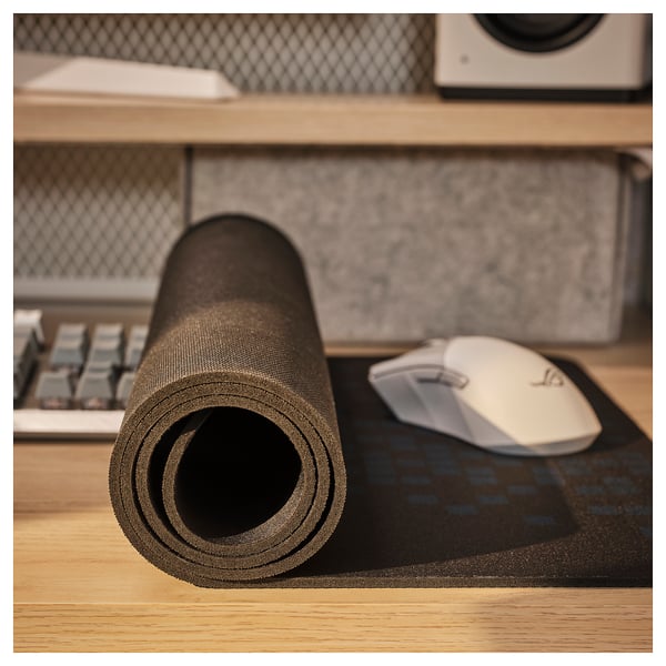 Black rolled-up wide gaming mouse pad with pixel pattern on wooden desk, white mouse near it.