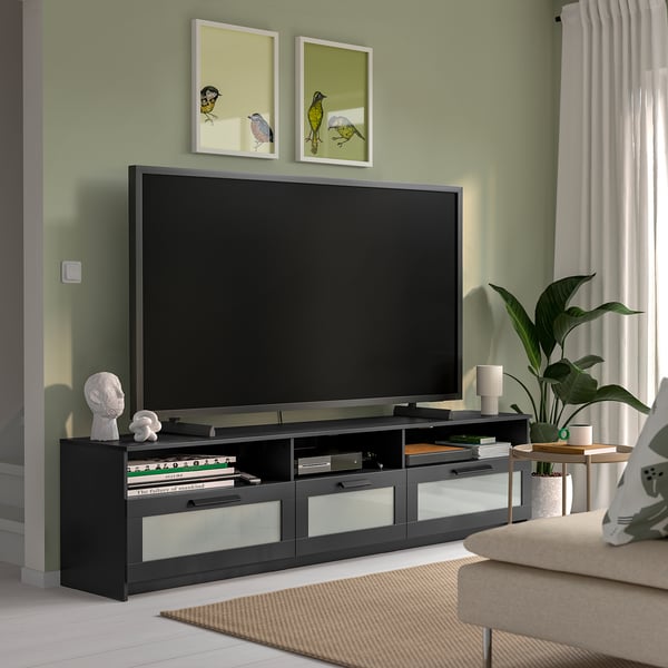 Modern living room with BRIMNES tv stand, sleek black and glass design, large size fitting big tv, drawers for storage, decorative items, and plant.