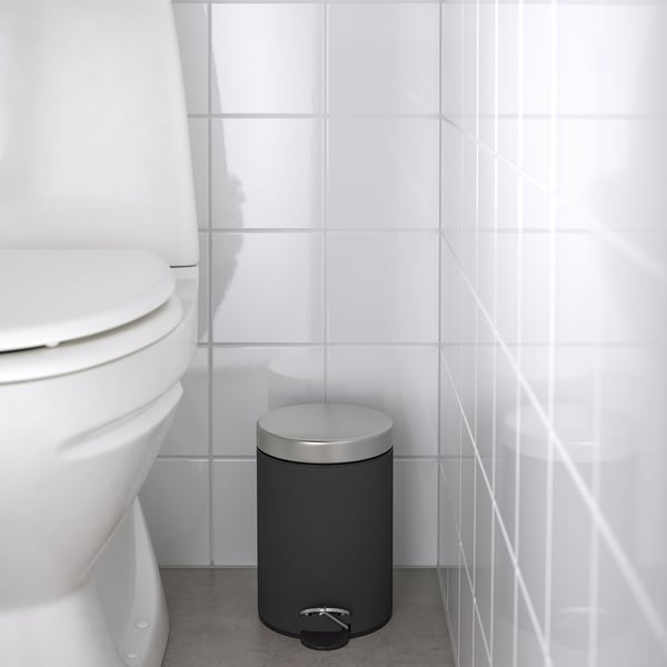 Black pedal bin beside a white toilet, set against white-tiled walls.