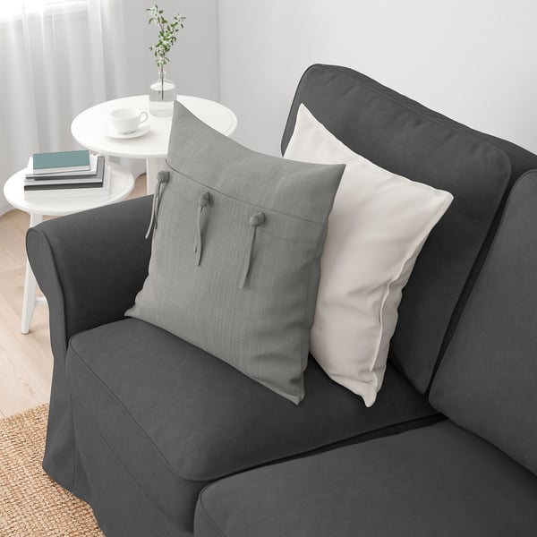 Dark grey sofa with cushions, on wooden floor near white table with books and cups.