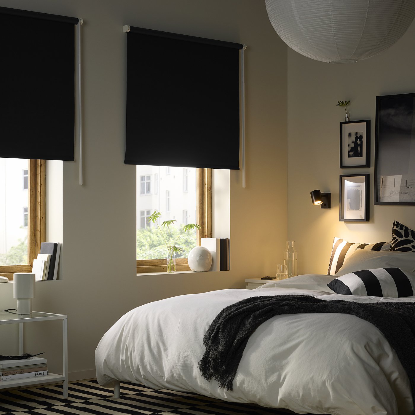 Black FRIDANS blinds cover large windows in cosy bedroom with double bed.