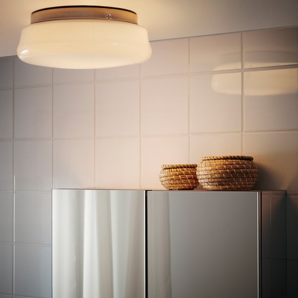 A modern bathroom with a round ceiling light providing diffused light, and two wicker baskets atop a cabinet.