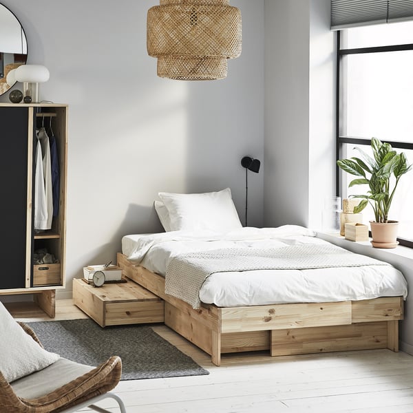 Modern bedroom with a natural wood GLAMBERGET extendable bed, white linens, hanging wicker light, and potted plant by the window.