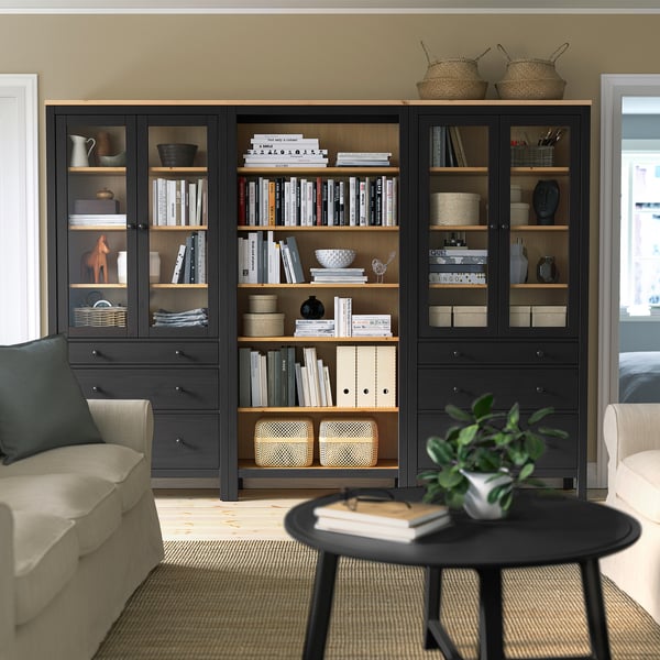 A large HEMNES bookcase in black with wooden shelves. Its filled with books & decor, standing between a couch and a table, adding warmth to the room.