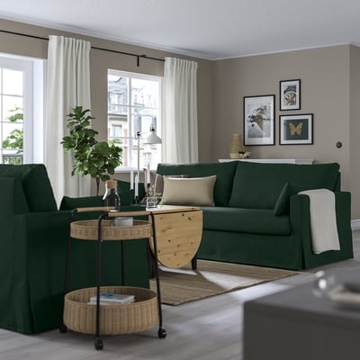Modern living room with dark green HYLTARP sofa, cushions, large windows, plant, coffee table, and wall art.