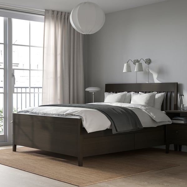 Modern bedroom with dark wood bed, soft lights, grey linens & large window.