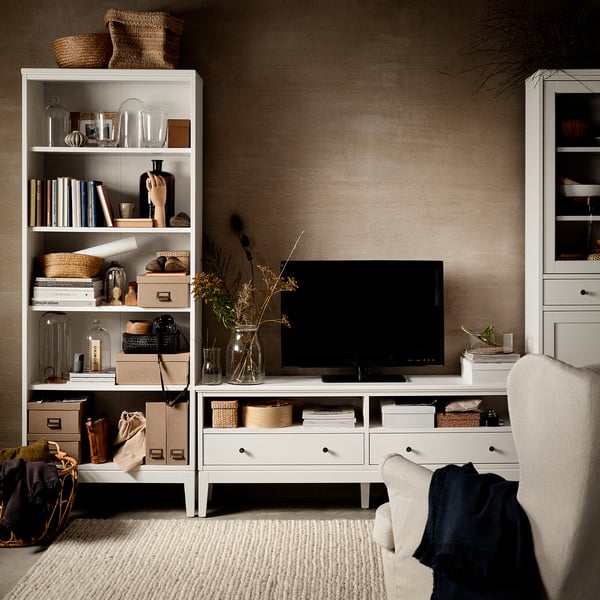 Modern living room with white IDANÄS tv stand, flat screen, books, vases, and beige chair.