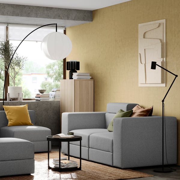 Grey JÄTTEBO modular sofa with side table, lamp, cabinet, art, and window view.