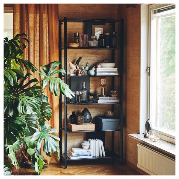 Black metal and bamboo JÄTTESTA shelf, filled with decorative items. Large green plant by window, warm-toned curtains.