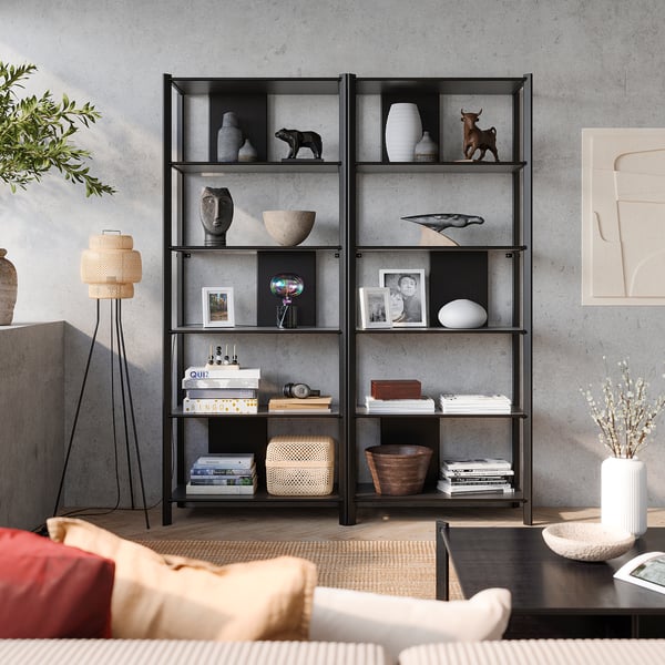 Modern living room with black shelves, vases, photos, books, plants, and red cushion.