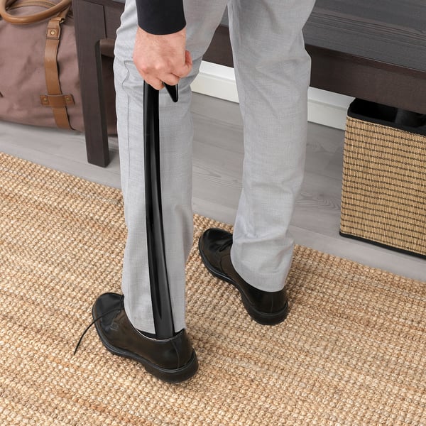 Person using shoehorn on mat near bench with bag.