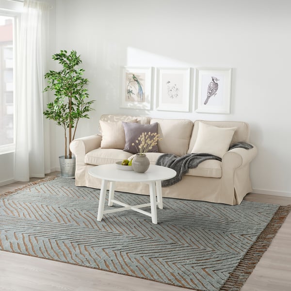 The living room a beige KLAPPERSTARR rug, larger than the white coffee table and cream sofa, with intricate textured wool and cotton design.