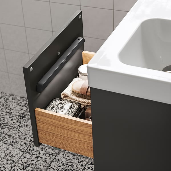 Open wooden drawer reveals soft lighting, organising clothes and accessories in a bathroom setting, showcasing modern convenience and storage.