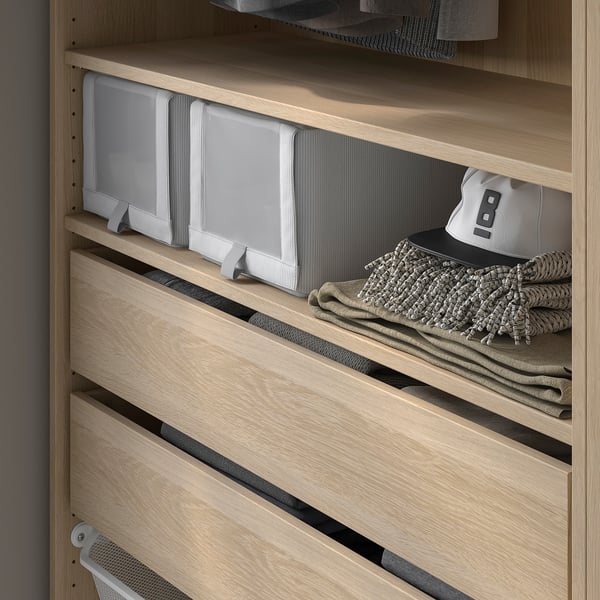 A wooden closet interior with light-colored KOMPLEMENT shelves. One shelf holds grey textured skubb boxes and folded clothes.