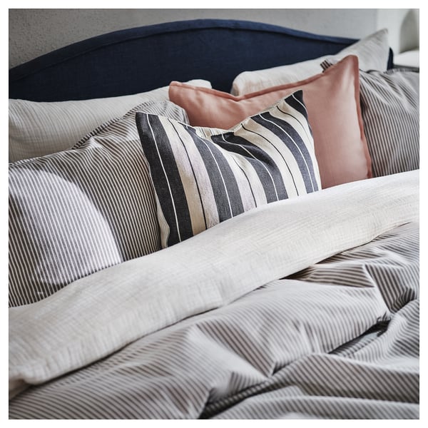 Bed with grey and white striped pillows, one pink, on a navy headboard.