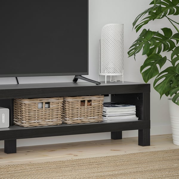 BLACK tv bench with woven baskets and cds, next to a large leafy plant.