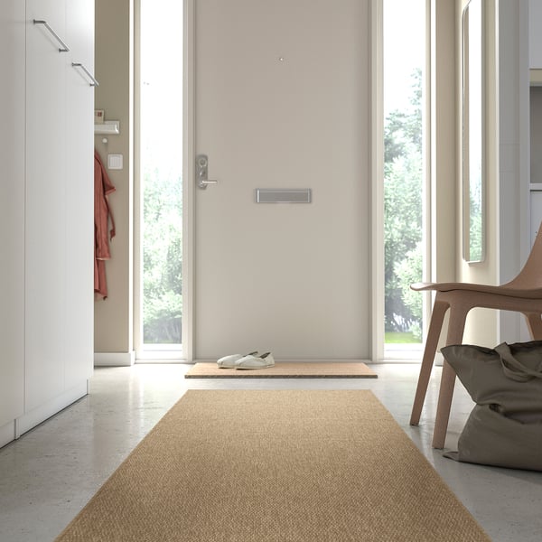 Light beige LÄTTBETONG rug in entryway, near door, smaller than chair.