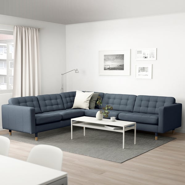 Modern living room with l-shaped blue fabric sectional sofa, white coffee table, floor lamp, rug, and wall art.