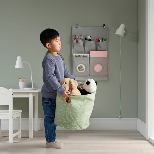 A young boy holding a green polka dot storage bag with two stuffed animals.