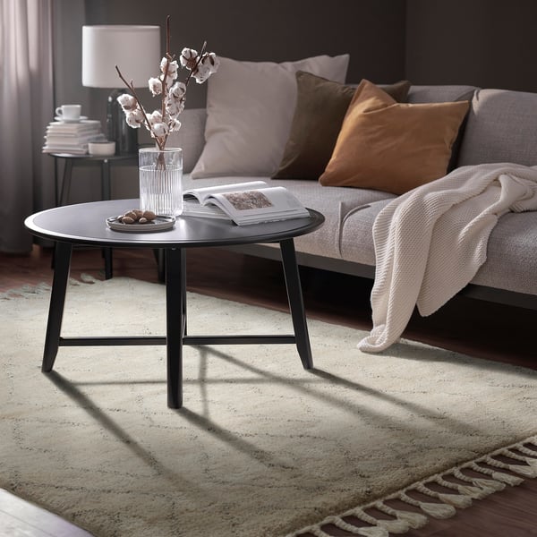 Cosy living room with black coffee table, white flowers, grey sofa, and warm lighting.