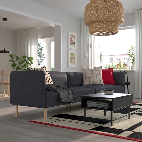 Modern living room with grey modular sofa, throw pillows, coffee table, pendant lamp, plants, and framed pictures.