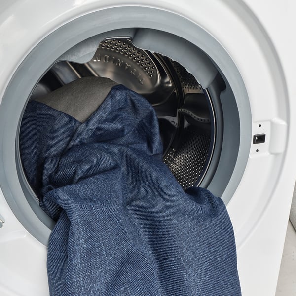 A washing machine loaded with dark clothes, showcasing its white drum and a grey lid with the brand indens visible.