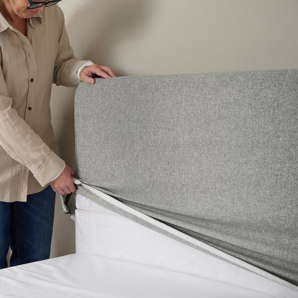 Person adjusting a padded, machine-washable headboard cover on a bed.