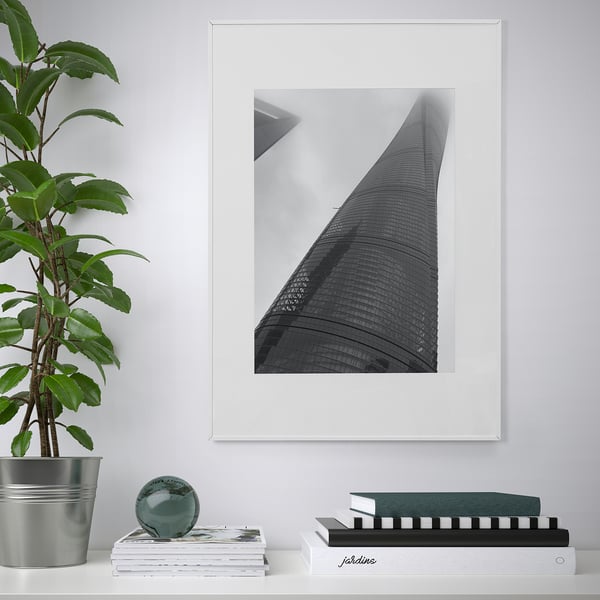 Modern living room with LOMVIKEN black & white skyscraper photo frame, metal edge, surrounded by books and green plant.