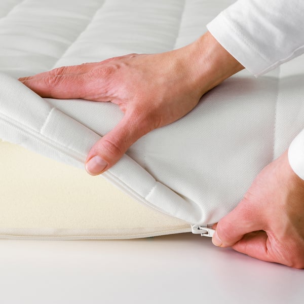Hands zipping up a white mattress, showcasing its removable cover for easy cleaning.