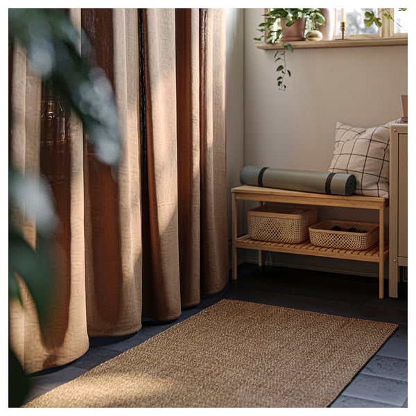 Calming indoor space with beige LYDERSHOLM rug, wooden bench, yoga mat, and curtained window.