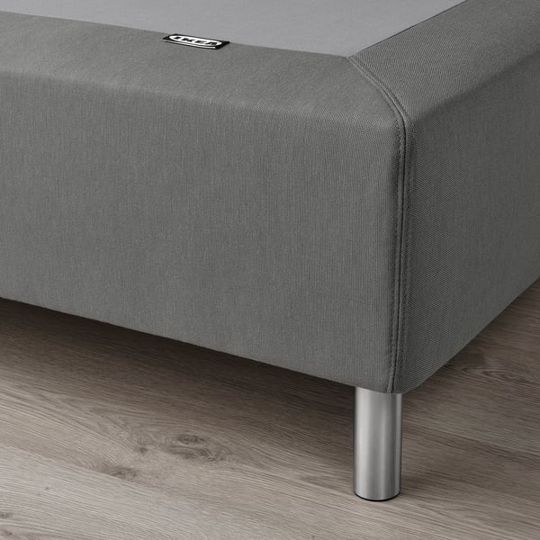 Grey upholstered bed base with metal legs on wooden floor.