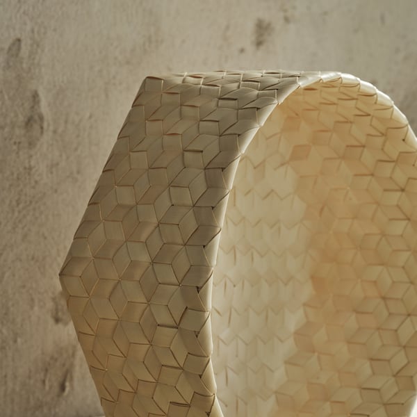 Handwoven basket with intricate hexagonal pattern, showcasing natural palmyra leaves, sits against a textured wall.