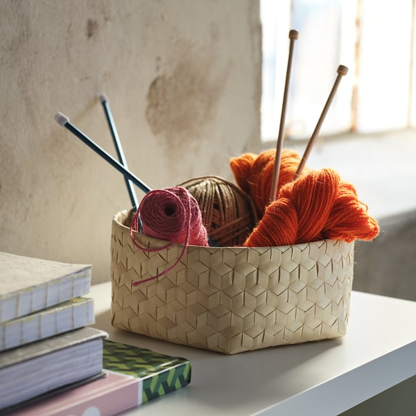 Basket on shelf with yarn, knitting needles, and crochet hooks, displaying a hand-braided natural pattern.