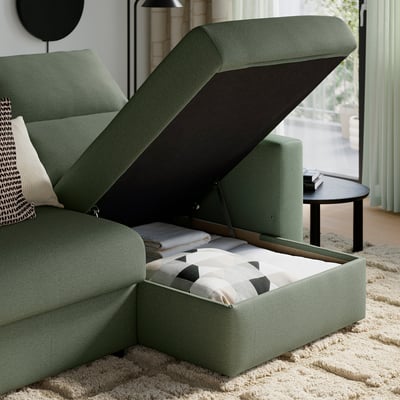Green sofa with open storage compartment filled with pillows and blankets.