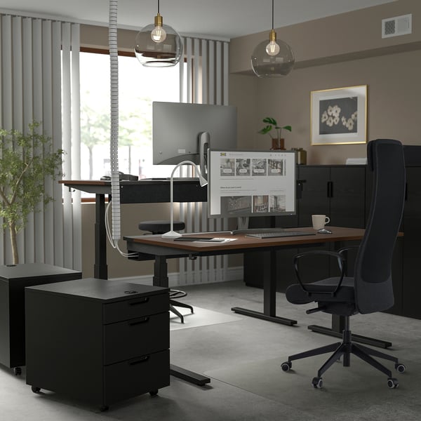 Home office with ergonomic chair, desk, dual monitors, lights, plant, and art.