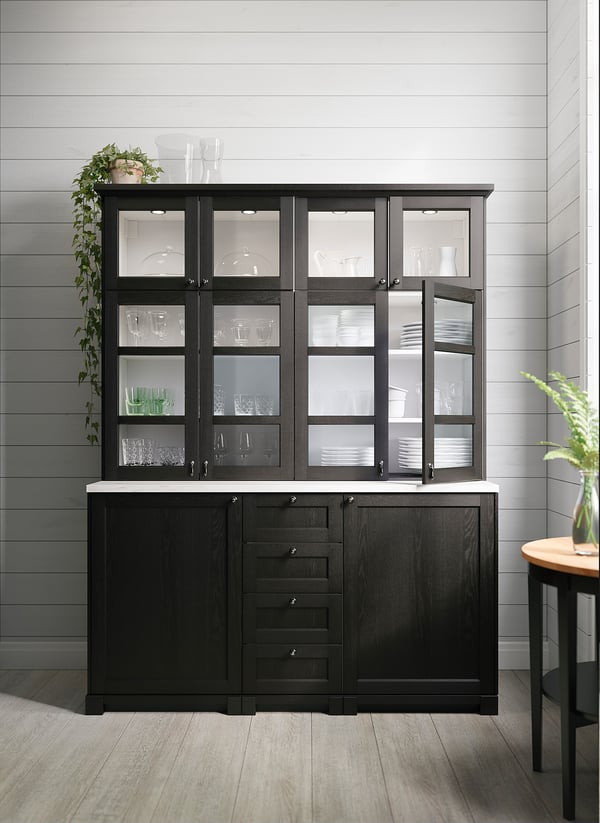 Modern black kitchen cabinet with glass doors, illuminated by MITTLED lights, displaying dishes and glasses.